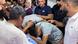Dos jóvenes lloran inclinados sobre el cadáver cuberto por una tela azul mientras varias personas intentan consolarlos con la mano en la espalda. Dos jóvenes lloran inclinados sobre el cadáver cuberto por una tela azul mientras varias personas intentan consolarlos con la mano en la espalda.