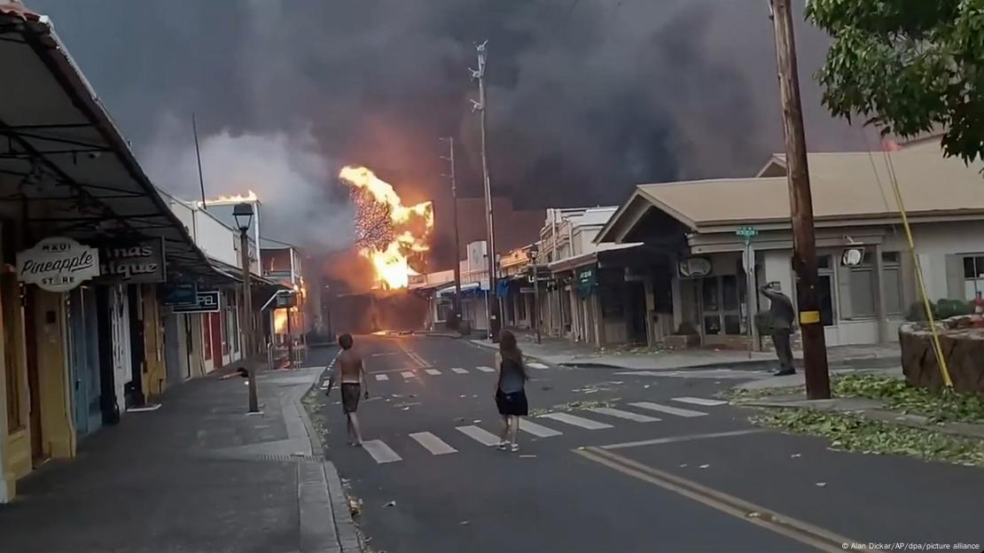 Incendios azotan Lahaina, en Hawái.  El fuego se ve en el horizonte de un cielo totalmente cubierto por humo, mientras las personas tratan de encontrar un lugar seguro.