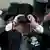 A spectator wearing a cylinder hat watches a horse race through his binoculars