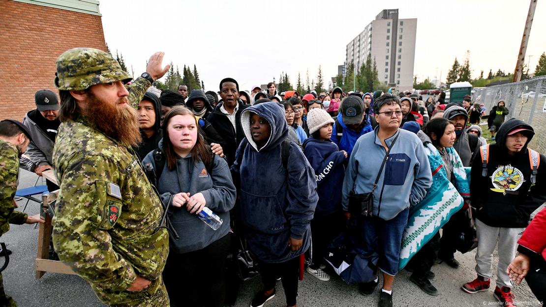 La gente hace cola fuera de una escuela local de la ciudad de Yellowknife para registrarse para ser evacuados, a medida que los incendios forestales amenazan los Territorios del Noroeste.