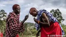 A young Maasai man paints the head of his friend using a stick and the traditional red ochre pigment as they prepare to take part in the Eunoto ceremony in a remote area near Kilgoris, Kenya on August 18, 2023. Hundreds of young Maasai take part in the Eunoto ceremony, a rite of passage that marks the transition from Moran (young warrior) to adulthood as junior elders. This ceremony is held by every clan once in a generation -every 8 to 10 years- and marks a new age-set. Eunoto, Enkipataa and Olng'esherr are the three main Maasai rites of passage that have been inscribed since 2018 on the Urgent Safeguardiang List of Intangible Cultural Heritage by UNESCO. (Photo by Luis Tato / AFP)