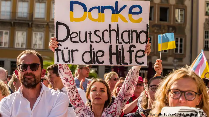 （社民党集会人群照片，图中一女子手举牌子，上面写着：感谢德国的帮助）战争难民在2023年8月一场社民党集会上感谢德国提供帮助