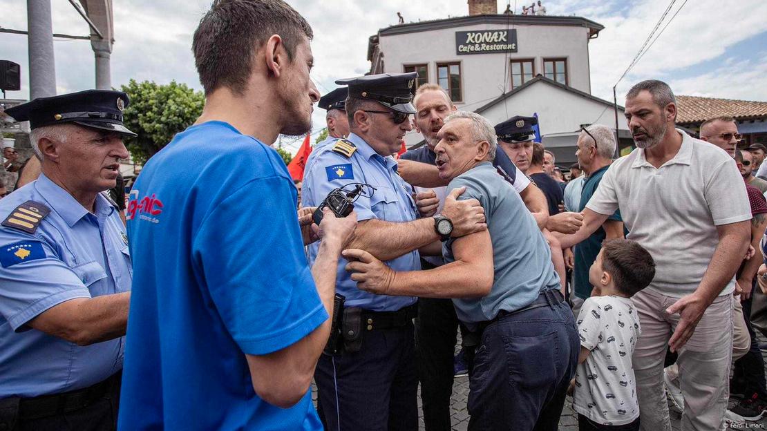 Journalist Vullnet Krasniqi (dressed in a blue T-shirt) speaks as a police officer and civilian try to restrain an angry protester, Prizren, Kosovo, August 11, 2023