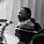 Black and white picture of US civil rights activist, Martin Luther King Jr, speaking into a microphone. 