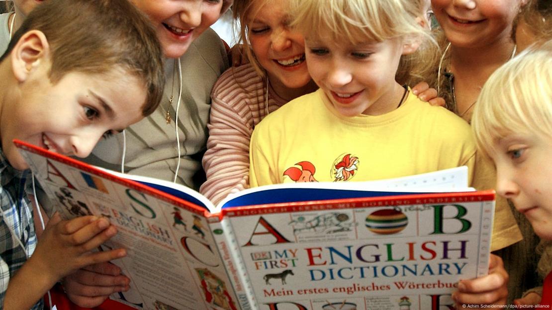 Cheerful German primary school pupils reading an English dictionary together