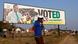 A man gestures while speaking on a cellphone as he walks past a banner of the ruling ZANU-PF party's President Emmerson Mnangagwa