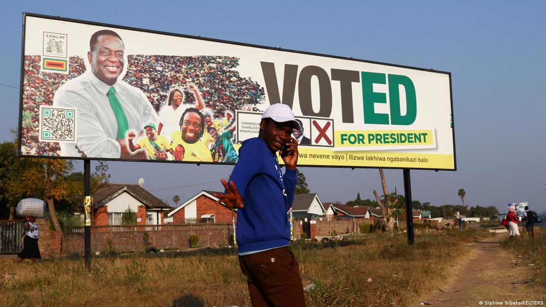 A man gestures while speaking on a cellphone as he walks past a banner of the ruling ZANU-PF party's President Emmerson Mnangagwa