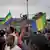  A military vehicle passes by people celebrating and waving Gabon's flag