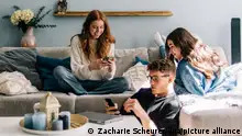 ILLUSTRATION - Teenager sitzen am 25.05.2023 in Berlin zusammen im Wohnzimmer auf einer Couch und schauen auf ihre Smartphones (gestellte Szene). Foto: Zacharie Scheurer || Modellfreigabe vorhanden