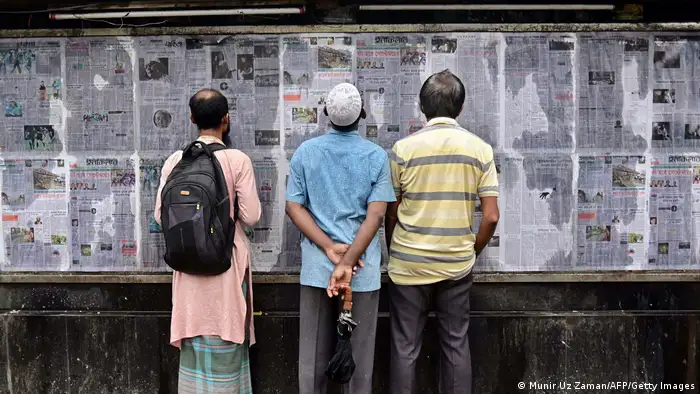 People stand in the street and read Bangladesh's local newspapers pasted along a wall in the capital Dhaka in September 2023 ahead of elections.