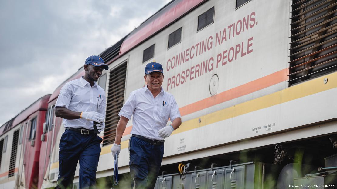 Two men, one Kenyan and the other Chinese, walking alongside a train