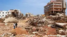 TOPSHOT - Men walk past debris of buildings caused by flash floods in Derna, eastern Libya, on September 11, 2023. Flash floods in eastern Libya killed more than 2,300 people in the Mediterranean coastal city of Derna alone, the emergency services of the Tripoli-based government said on September 12. (Photo by AFP) (Photo by -/AFP via Getty Images)