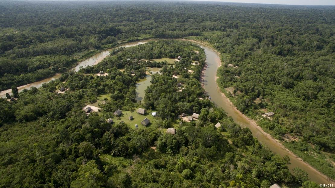 Vista aérea de uma aldeia na beira de um rio, cercada de floresta