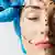 Ein Chirurg markiert mit schwarzem Stift das Gesicht einer Frau vor einer Schönheit-OP. Nasen, Kinn und Stirn sind markiert. 