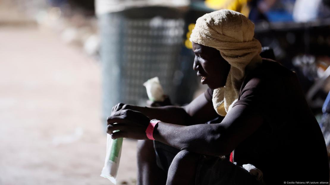 Lampedusa | Italien | Migranten: Ein Mann mit einem Handtuch um den Kopf hockt (vermutlich am Straßenrand)