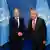 Zwei Männer in Anzügen geben sich die Hand und lächeln in die Kameras, im Hintergrund das Zeichen der Vereinten Nationen mit einer stilisierten Weltkarte