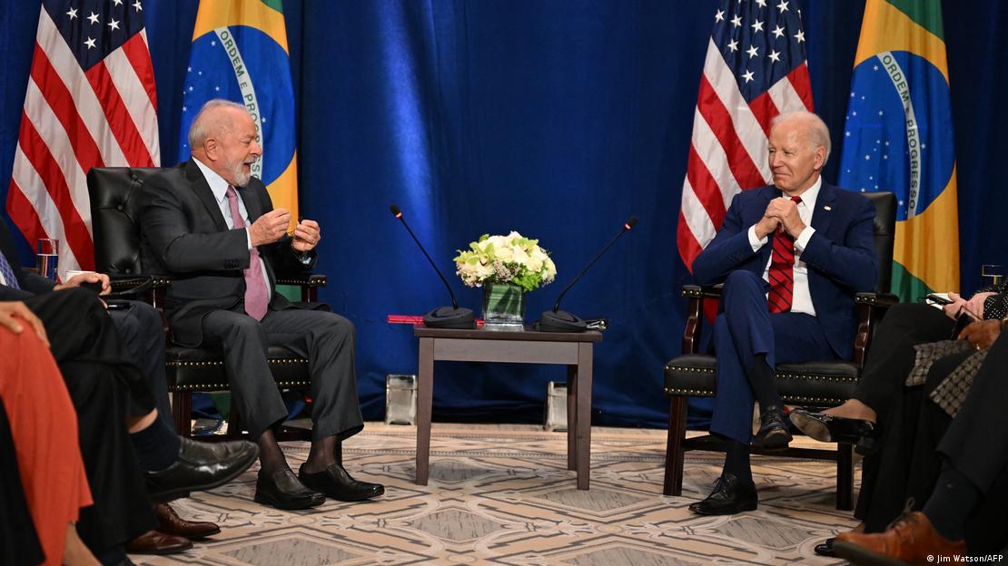 Lula e Biden sentados conversando em sala com bandeiras dos EUA e do Brasil
