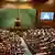Visão geral do Parlamento da Índia em dia de sessão: uma sala com carpete verde e bancos de madeira dispostos em um semicírculo