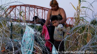 A woman and child make their way through tangled barbed wire on the US-Mexico border
