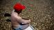 A man with a red cap, his back turned to the camera, sits at the bow of a ship holding a paddle in his hands. Around him, countless dead fish float in the murky water. 