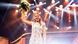 Eva Brockmann smiles as she stands on stage wearing a white dress and a golden crown and raises a bouquet of flowers with her right hand Eva Brockmann smiles as she stands on stage wearing a white dress and a golden crown and raises a bouquet of flowers with her right hand