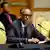 Rwanda's President Paul Kagame gestures as he sits at a desk with a microphone in front of him