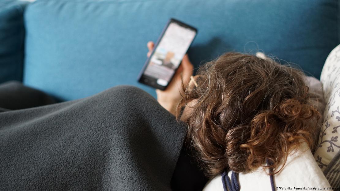 Una persona acostada en un sofá con un celular en la mano.