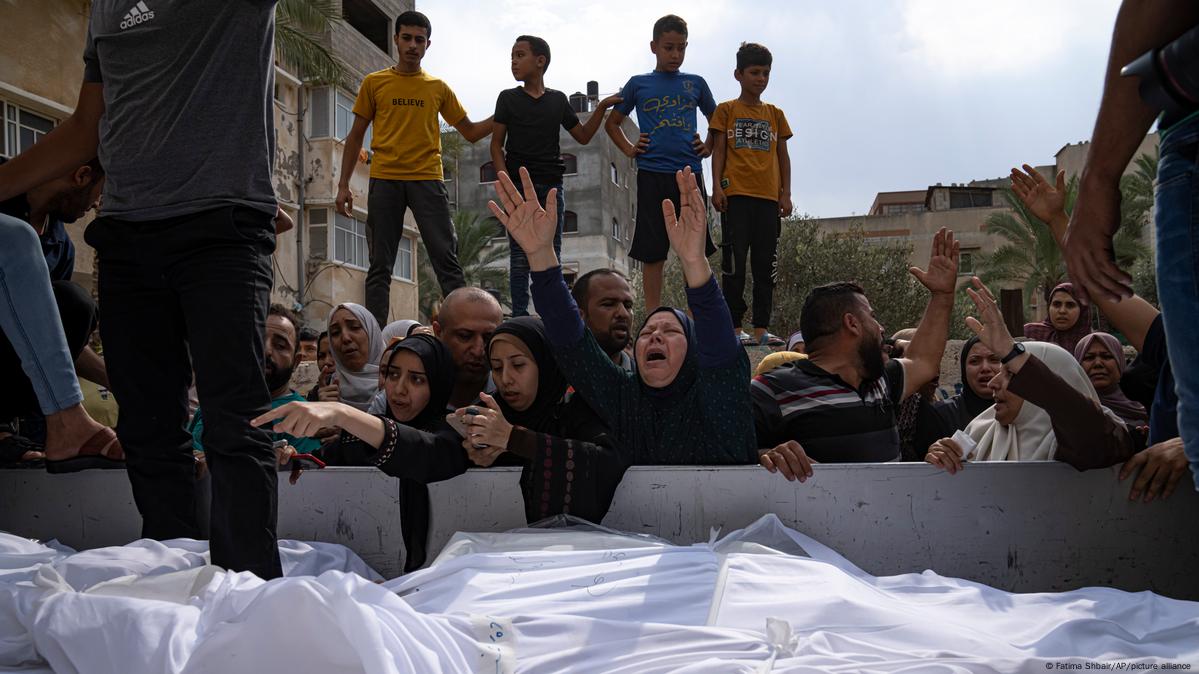 A imagem mostra pessoas em luto, aglomeradas, na Faixa de Gaza, em meio a corpos cobertos com panos brancos, de mortos após ataque aéreo de Israel.