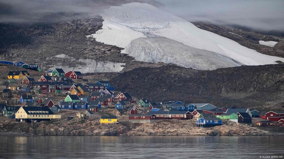 Panoramë e qytetit Inuit në Groenlandë me shtëpitë rrëzë malit dhe buzë liqenit si dhe akullnaja në shkrirje