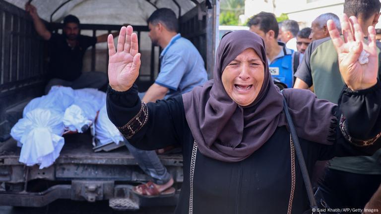 Une femme palestinienne lève les bras au ciel en pleurant devant un camion où sont chargés deux cadavres dans des sacs (photo prise le 10.10.2023)