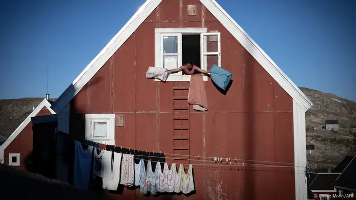 A woman stands at the open window in a red house and knocks out pillows