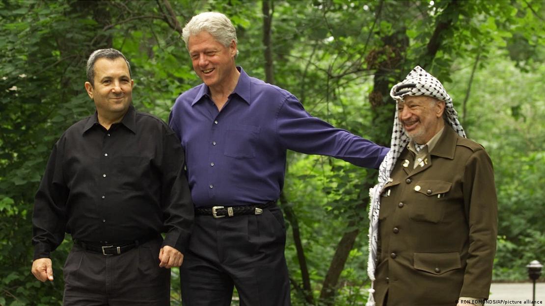 Kryeministri izraelit i atëhershëm, Ehud Barak, ish-presidenti Bill Clinton, dhe lideri i atëhershëm palestinez, Jaser Arafat - takim në Camp David, 11 korrik 2000- Presidenti Bill Clinton me krahët hapur mes Ehud Barak dhe Jaser Arafatit
