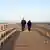 An elderly couple seen from behind walks on a wooden pier