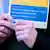 A woman's hands holding a flyer in the colors of the Ukrainian flag reading "Welcome to our job fair" in German and Ukrainian. The fair was organized by the Berlin Chamber of Industry and Commerce and the Employment Agency