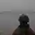 Ein Soldat am Flussufer, von dem wir nur den Rücken sehen, blickt auf einen anderen Soldaten im Boot 