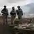 Minenräumer in Schutzkleidung und mit Stahlhelm stehen auf einem Feld hinter einem Haufen deaktivierter Antipanzerminen