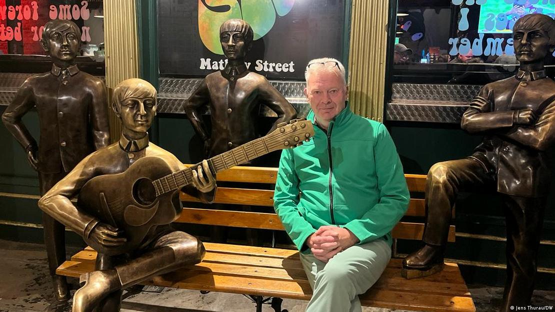 Jornalista Jens Thurau, da DW, posa para foto sentado em banco com estátuas de bronze dos Beatles.