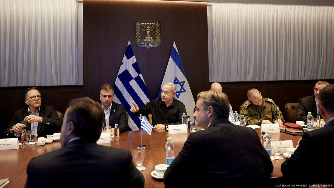 Eine Gruppe von Männern an einem Tisch vor einer griechischen und einer israelischen Flagge