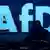 Logo AfD-a ispisan svijetlo plavim slovima na tamnoplavoj pozadini. Ispred njega sjedi osoba kojoj se vide samo leđa i glava u tami.