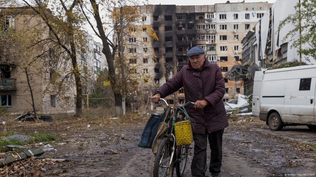 Възрастен мъж бута велосипед в Авдеевка пред разрушен блок Възрастен мъж бута велосипед в Авдеевка пред разрушен блок