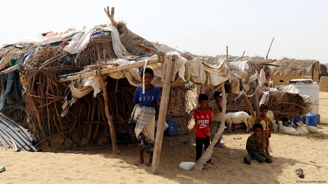 Kinder stehen und sitzen vor einer notdürftigen Hütte aus Reisig, Stöckern und Lumpen im Sand Kinder stehen und sitzen vor einer notdürftigen Hütte aus Reisig, Stöckern und Lumpen im Sand