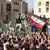 Multidão durante protesto, com homens sobre cerca portando uma bandeira do Egito
