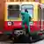 Ein Wagen der Berliner S-Bahn vom Modell 485 steht auf einem Gleis. Ein Mann in grünem Arbeitsoutfit und Kappe klettert vorn zu den Fenstern, ein anderer Mann in Anzug und mit blauem Helm steigt hinten aus einer Tür. 