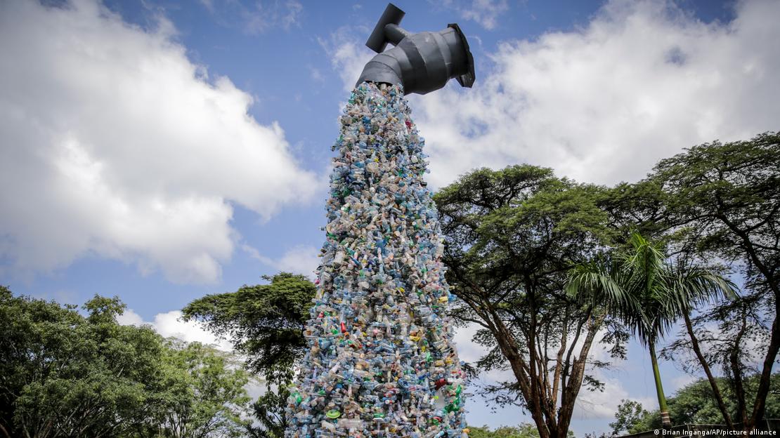 Escultura gigante simula uma torneira. Dela, em vez de água sai produtos plásticos