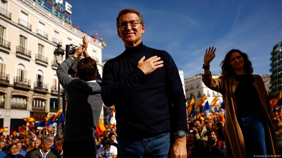 Feijóo se lleva la mano al corazón mientras Ayuso saluda sonriente detrás de él.