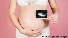 A happy expectant mother shows an ultrasound image of the fetus on camera. Prenatal ultrasound screening. close-up of the abdomen of a young pregnant woman holding a sonogram of an unborn child