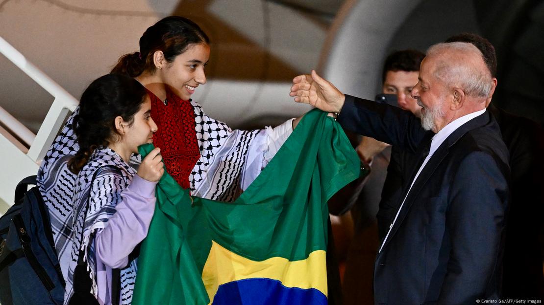 Duas meninas com a bandeira do Brasil são recebidas por Lula na saída de um avião.