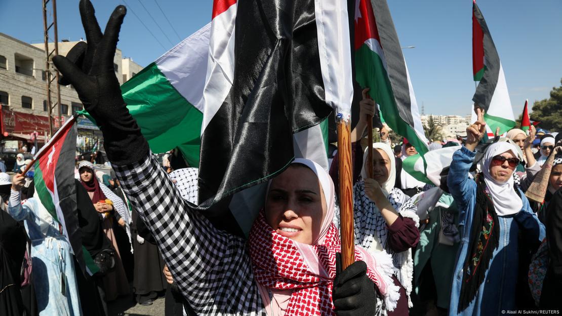 Mulher segurando uma bandeira da Palestina faz sinal de vitória com os dedos durante um ato pró-Palestina