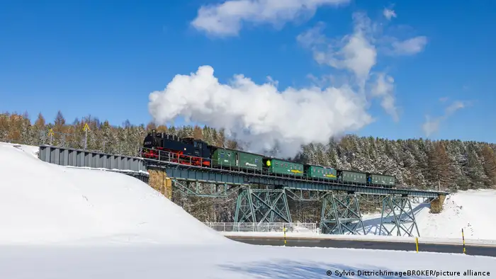 Schmalspurbahn mit Dampflokomotive in schneebedeckter Landschaft, Erzgebirge, Deutschland 