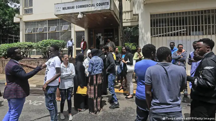 More than a dozen people stand in front of a Nairobi court and talk to each other.